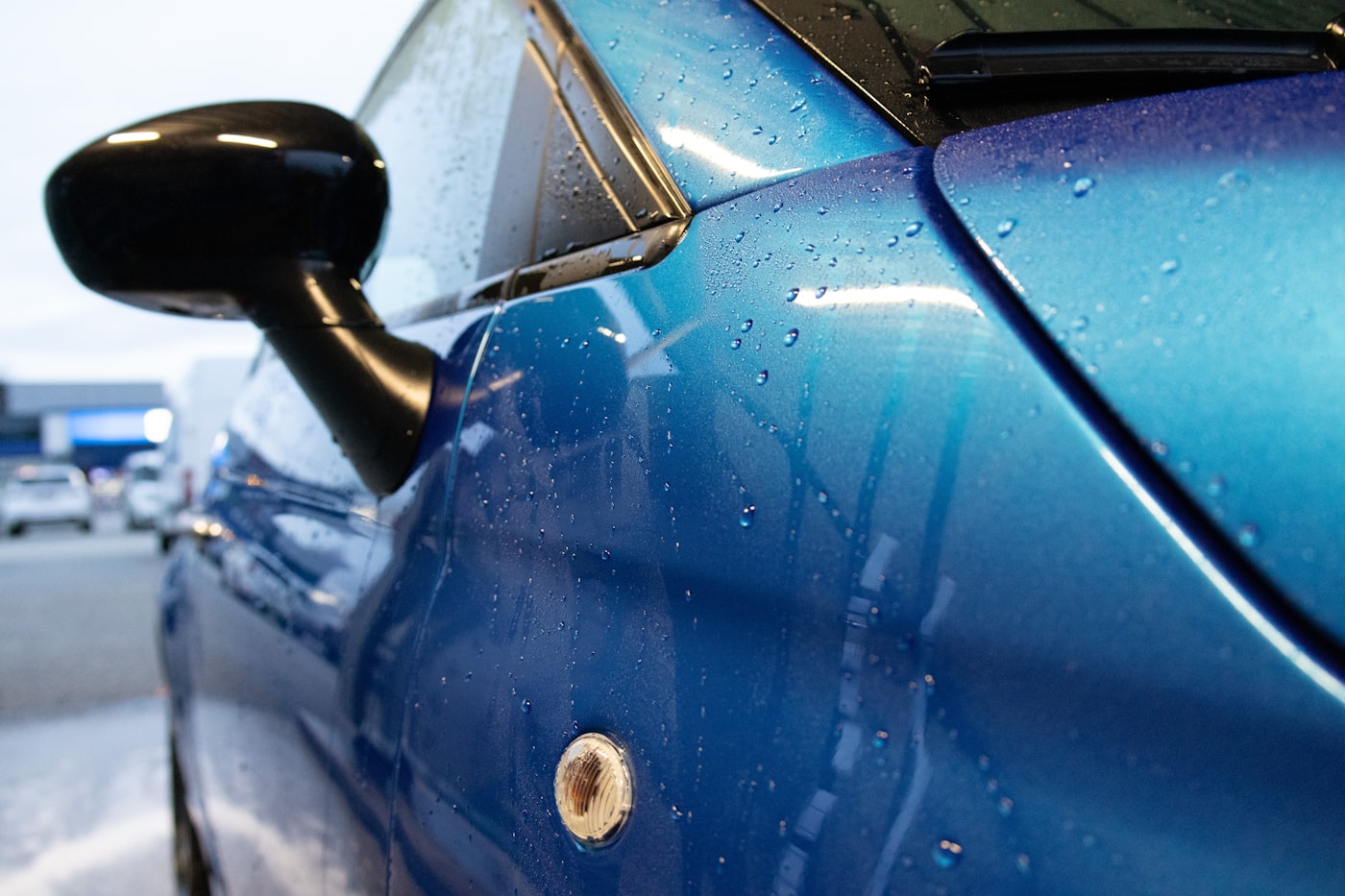 Nahaufnahme einer blauen Fahrzeugflanke mit Wassertropfen